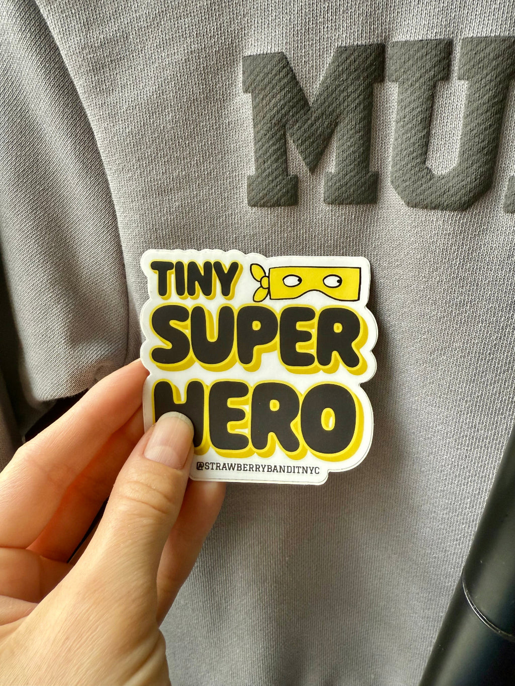 Colorful Tiny Superhero Sticker by Strawberry Bandit featuring a small superhero character on a vibrant background. Black and Yellow.